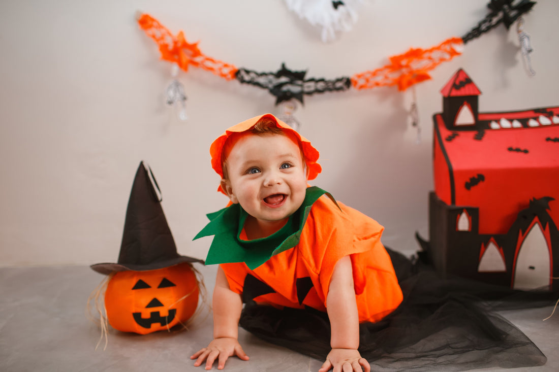 A baby in a pumpkin costume lying on a soft cream blanket