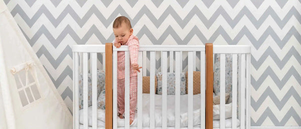An image of a baby standing inside a crib and leaning over the railing