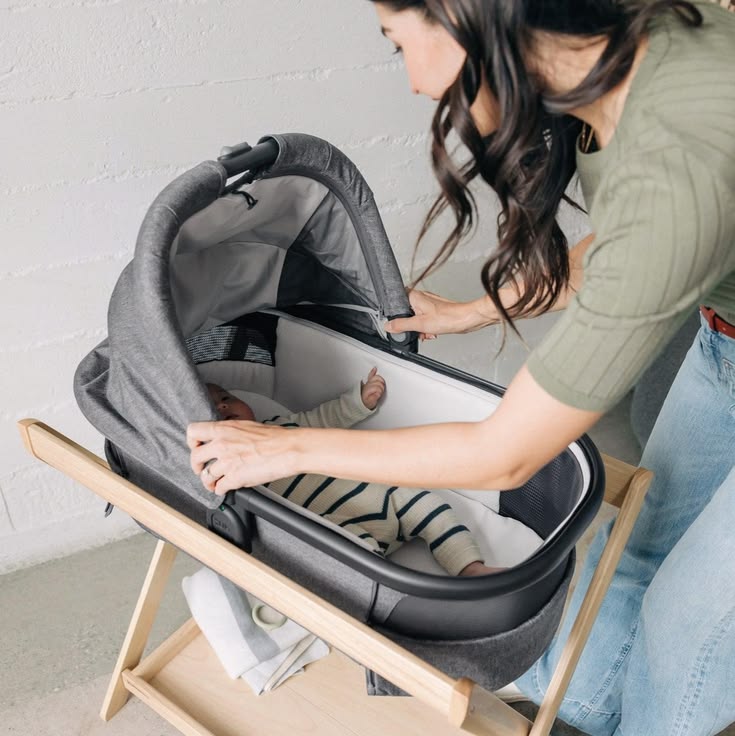 An UPPAbaby bassinet on its stand beside a made bed
