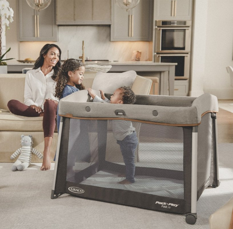 A toddler standing in a Graco Pack n Play in the living room