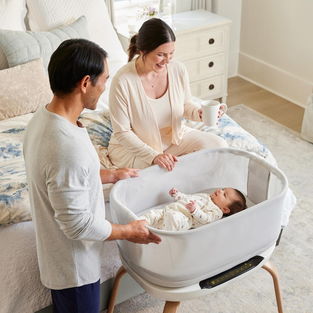 Parents smiling at their baby in a Graco SmartSense bassinet