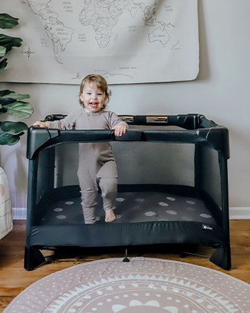 Smiling toddler standing in a 4moms Breeze playard