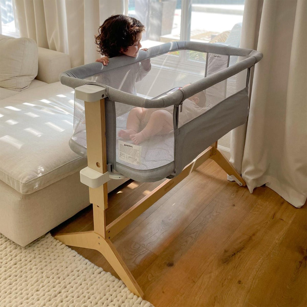 Toddler peeking into a Newton bedside bassinet