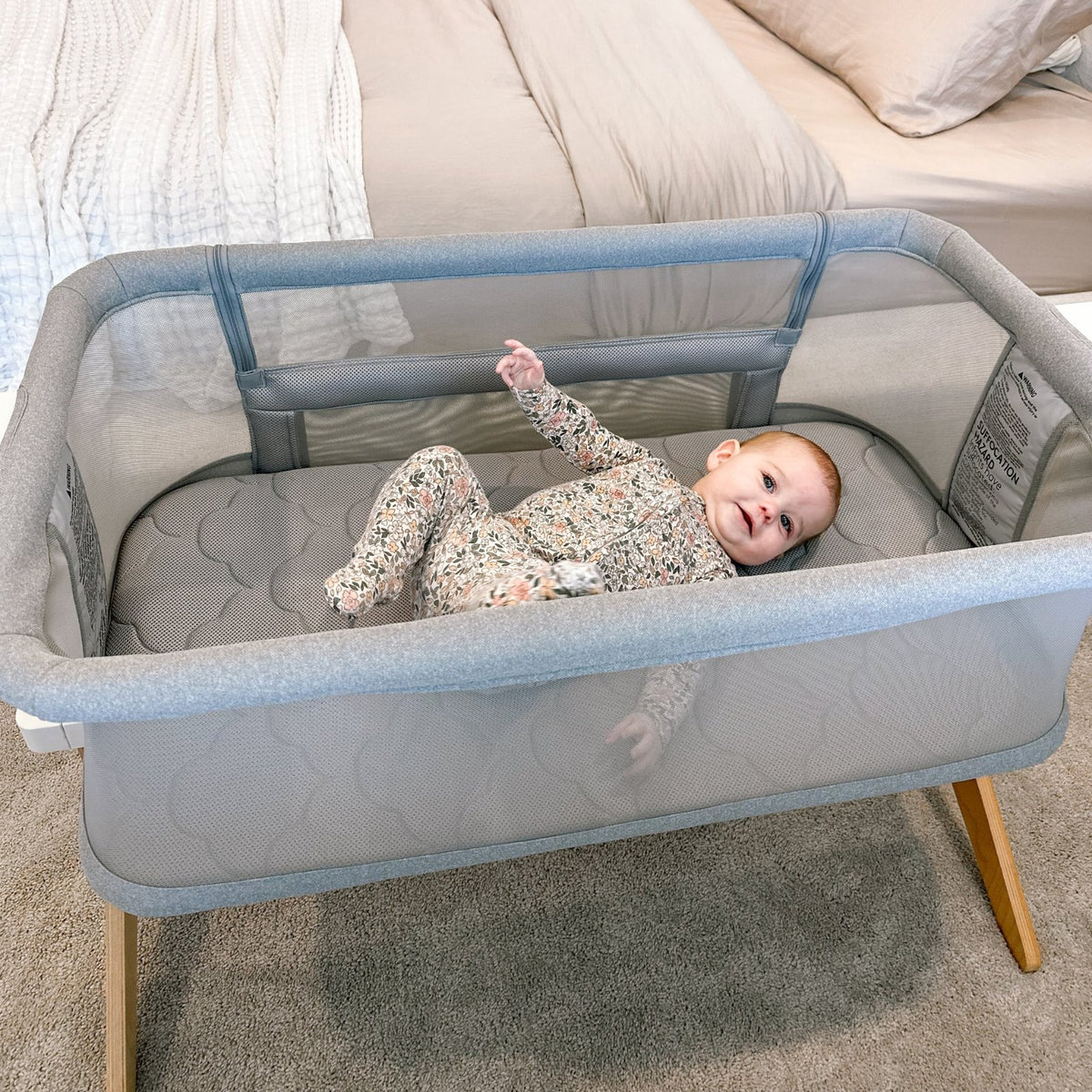 A baby lying in a Newton Baby bedside bassinet