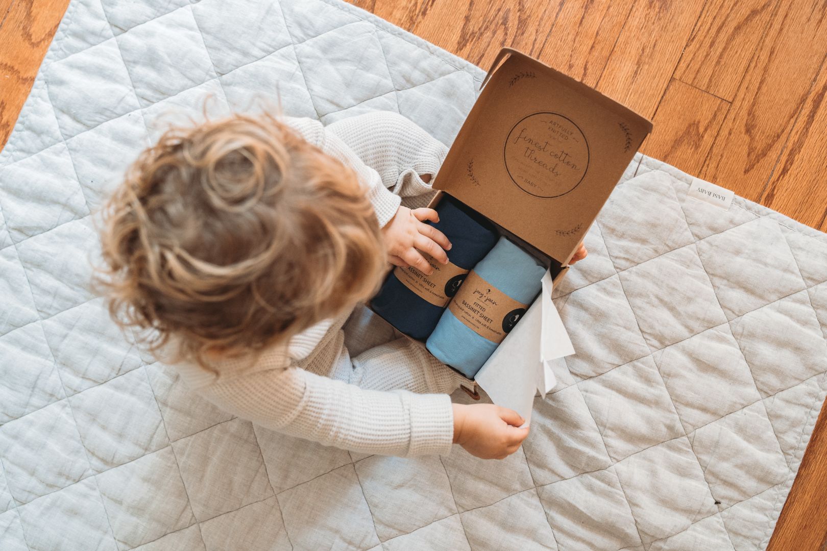 Toddler opening a Joey + Joan gift box of bassinet sheets