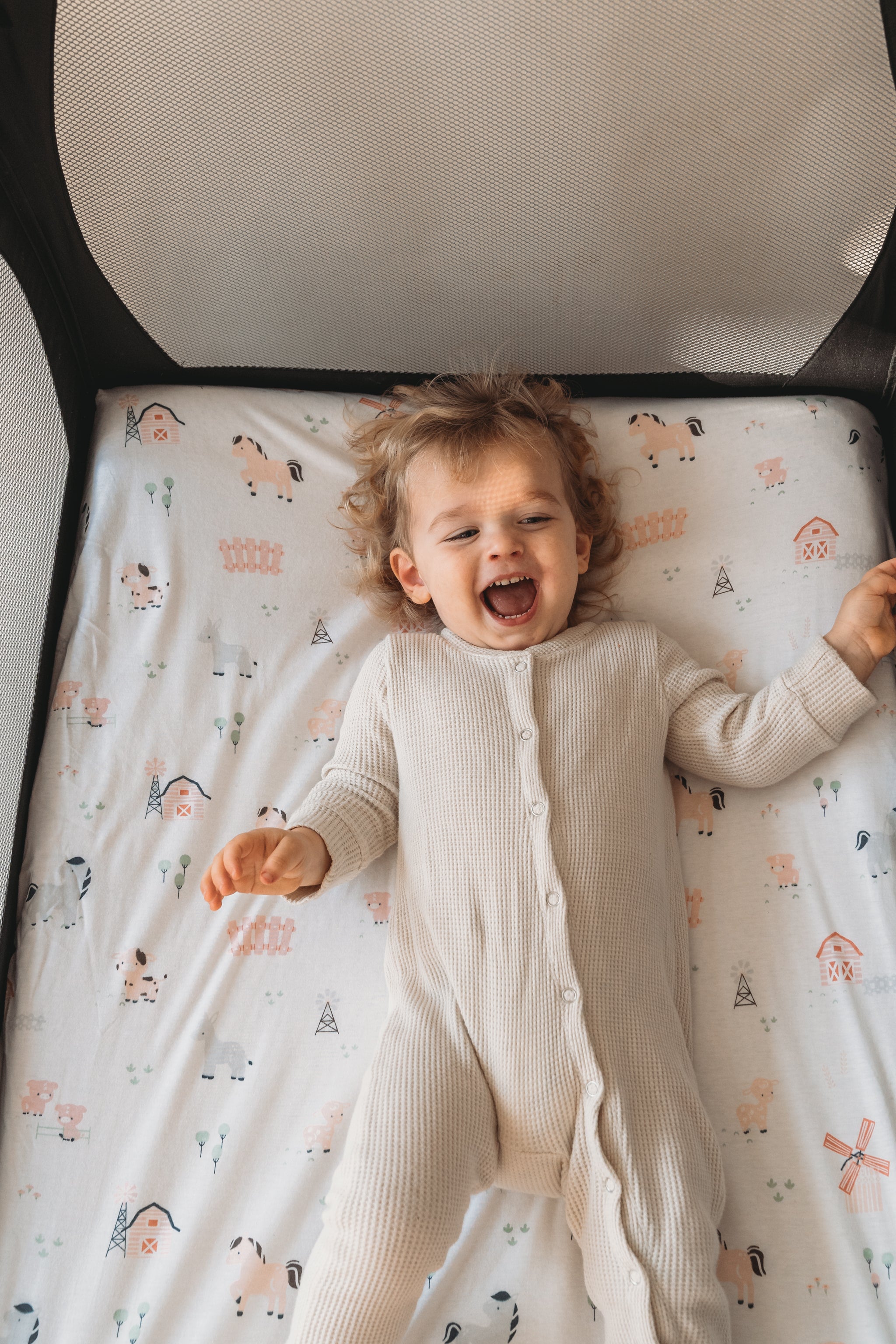 Baby laughing on a Joey + Joan farm-print playard sheet