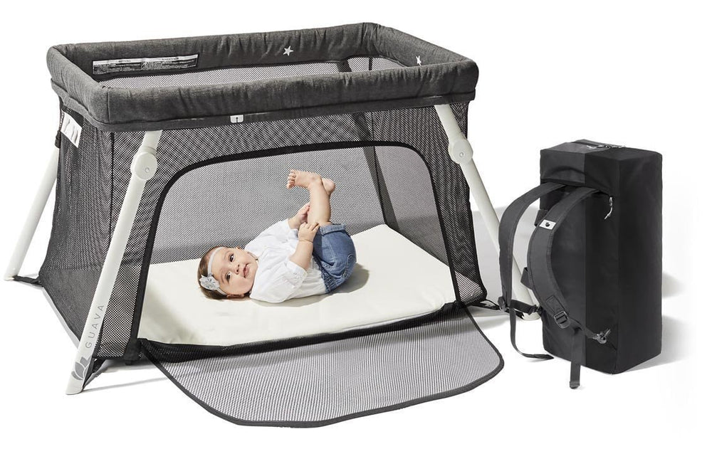 Baby lying in a Guava Lotus Travel Crib beside its travel backpack