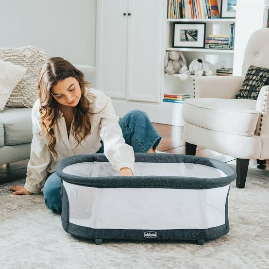 Mother reaching into a Chicco LullaGo bassinet in her living room