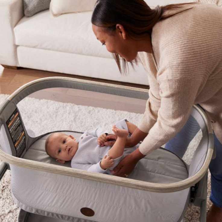 A mother laying her baby down in a Maxi-Cosi bassinet