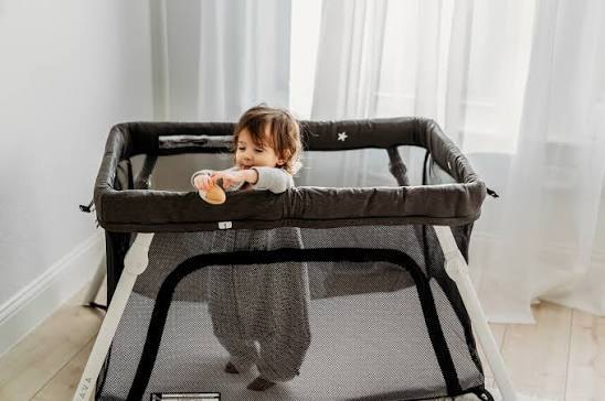 Toddler standing in a Guava Lotus Travel Crib