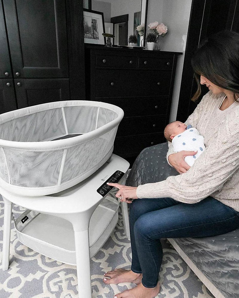 Mother holding her newborn beside a 4moms mamaRoo Sleep bassinet