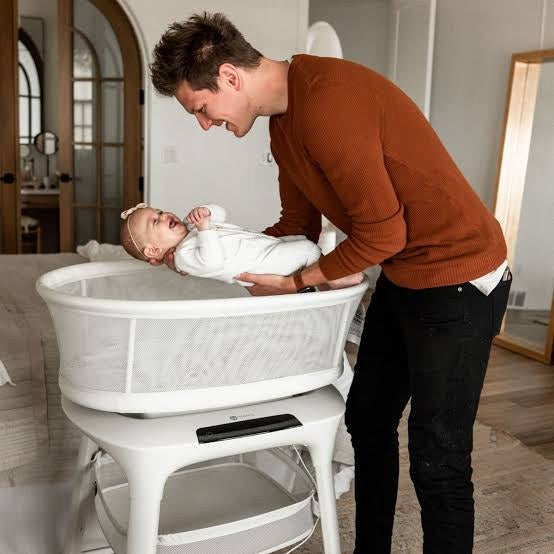 Parent lifting a baby from a 4moms mamaRoo Sleep bassinet