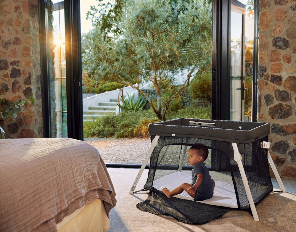 Toddler sitting in a Guava Lotus Travel Crib at sunset